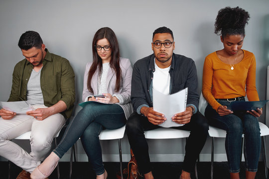 Worried and stressed man holding his resume sitting with other candidates waiting for the job interview in office - diverse young group of candidates waiting for a job interview