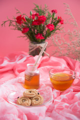 Lemon tea in transparent cup with vanilla cookies on saucer served with sugar cube and honey in mug on pink tone and flower for Valentine's  background