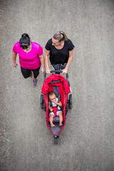 View from above of Two women in their 30s walking and talking together on a trail with pushing a baby stroller. Looking down from above