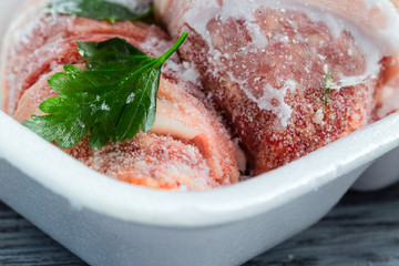 Frozen meat in hoarfrost in a plastic tray with a leaf of parsley