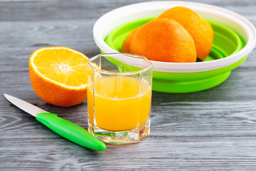 Freshly squeezed orange juice and oranges on a gray wooden table.