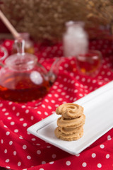 Tea pot and tea cup on wood table with honey and suagr in mag with flower basket on red cloth napkin, with butter cookies and brownies