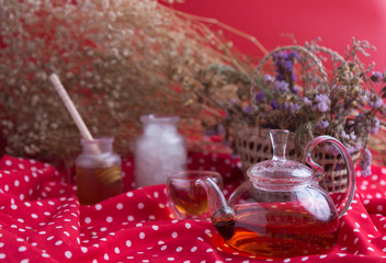 Tea pot and tea cup on wood table with honey and suagr in mag with flower basket on red cloth napkin