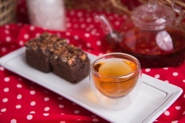 Tea pot and tea cup on wood table with honey and suagr in mag with flower basket on red cloth napkin, with butter cookies and brownies
