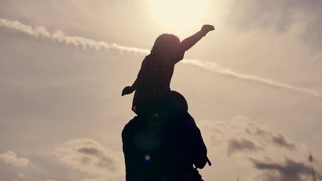 Happy family enjoying summer vacation in the Park at sunset. A small child sits on the neck of his father, a view from the back. Silhouette of a happy family.
