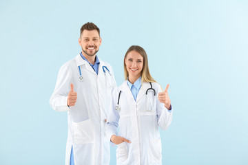 Fototapeta premium Male and female doctors showing thumb-up on light color background