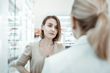 Fototapeta premium An anxiously looking picky woman attentively listening to the pharmacist.
