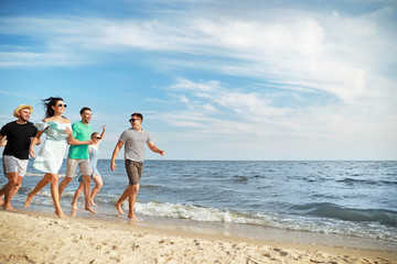 Happy friends running on sea beach at resort