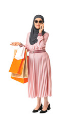 Beautiful mature Muslim woman with shopping bags talking by mobile phone on white background