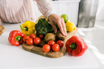 cropped view of pregnant woman touching kiwi near vegetables