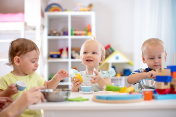 Babies playing together in kindergarten or creche. Kids sitting at table in nursery or daycare