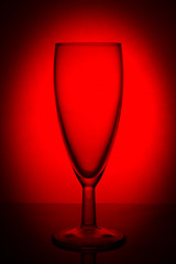 empty glass champagne glass on the lumen on a red background with a vignette