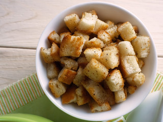 Crispy croutons in bowl on a wooden background.