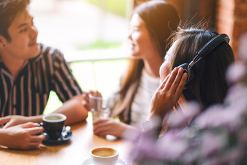 A beautiful asian woman enjoy listening to music with headphone while drinking coffee with friends