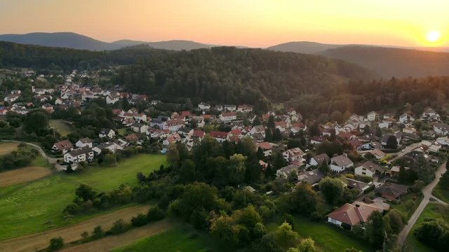 Village surrounded by beautiful hilly green landscape at a colorful sunrise, aerial footage 