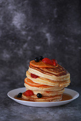 Pancake with orange, strawberry and blueberry on top with maple syrup. Sweet honey pour on pancake layer with grunge background
