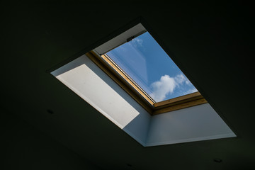 Looking up to the blue cloudy sky through modern square ceiling window