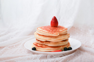 Many layers of pancake with strawberry and  blueberry on white dish  on sweet white cloth background