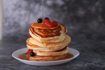 Pancake with orange, strawberry and blueberry on top with maple syrup. Sweet honey pour on pancake layer with grunge background