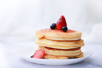 Many layers of pancake with strawberry and  blueberry on white dish  on sweet white cloth background
