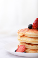 Many layers of pancake with strawberry and  blueberry on white dish  on sweet white cloth background