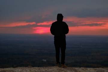 A lone man in a black jacket stands on top of a mountain in sunset time. Loneliness
