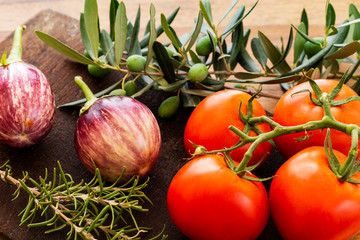 Rosa Bianca eggplants with red tomatoes on branch over a wooden board with green olives on branch...