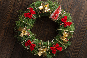 Christmas wreath decorated with red and gold bows and Christmas bell on a wooden background