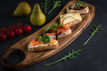 Four bruschettas lay on wooden board. Appetizers with tomato, mozzarella, pesto, salmon and roast beef.