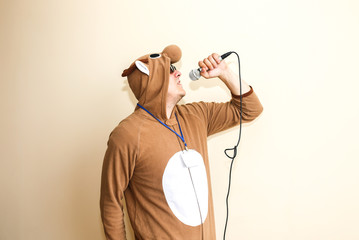Man in cosplay costume of a cow singing karaoke. Guy in the funny animal pyjamas sleepwear holding microphone. Funny photo.