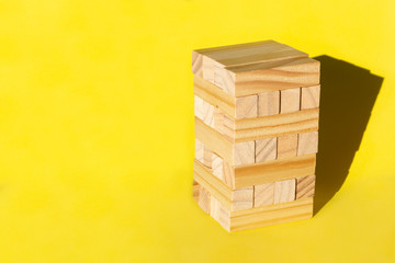 Wood jenga game with wooden block Stack tower on yellow background, manage risk and strategy.