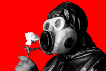 Man in the gas mask holding flower isolated on red background. Radiation influence. Environmental pollution. Chernobyl concept. Dangerous nuclear power. Ecological disaster.