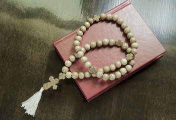 The holy bible and rosary beads on wooden background