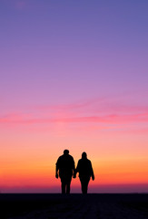 silhouette of man and woman walk holding hands in colorful sunset