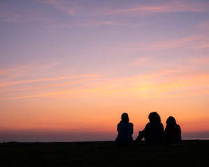 woman and two children sit watching colorful sunset