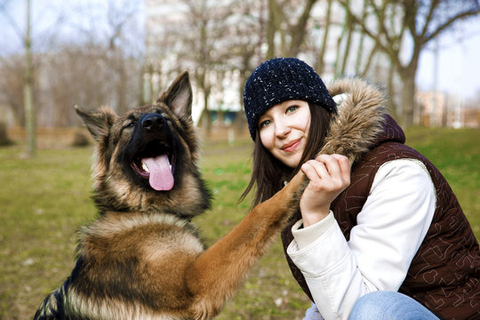   A Happy, Smiling Girl Is Holding A Dog Paw. A Cute German Shepherd Dog, Sheepdog  at the park