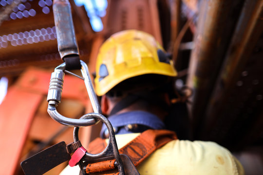 Construction worker welder wearing safety helmet, fall arrest harness clipping locking Karabiner attached retraceable energy shock absorber lanyard device on the back of his safety harness loop 