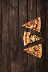 Cut into slices delicious fresh pizza with ham, olives, mushrooms and cheese on a dark brown retro boards. Top view with copy space. Pizza on the wooden table.