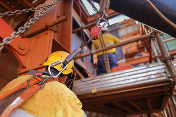 Welder wearing safety helmet, fall arrest construction harness using retractable anergy shock absorber safety lanyard device clipping on back harness loop and attached structure beam fall prevention 