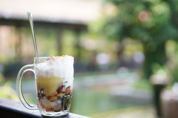 Street food, sweet dessert in tranparent jug with spoon. Many sweet bean and grass jelly in coconut milk on ice with nature background