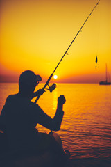 Silhouette of a fisherman fishing in sunset time on the open sea.