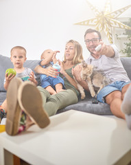 Young parents watching TV with baby boy and a dog.