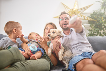 Young parents watching TV with baby boy and a dog.