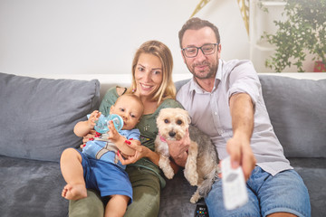 Young parents watching TV with baby boy and a dog.