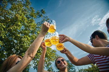 Group of young people enjoying and cheering beer outdoors.