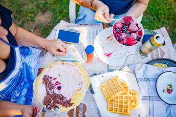People making a picnic with sweet waffle and pancaces in the garden.