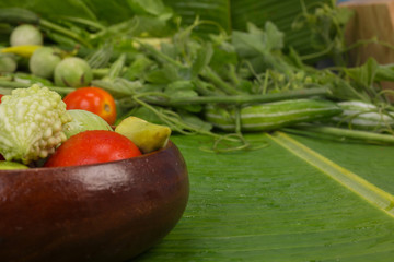 World Food Day Concept, bitter gourd, tomato, eggplant, okra in a wooden bowl and other vegetables placed in the background on a green banana leaf.
