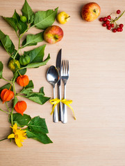 autumn themed place setting with a knife, spoon and fork, decorated with yellow flower, physalis branch
