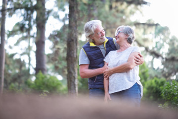 Happy senior couple with white hairs and large smiles in the woods. Casual clothing  for excursion. Enjoying and protect the nature