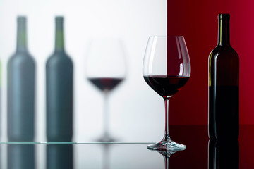 Bottles and glasses of red wine on a black reflective background.